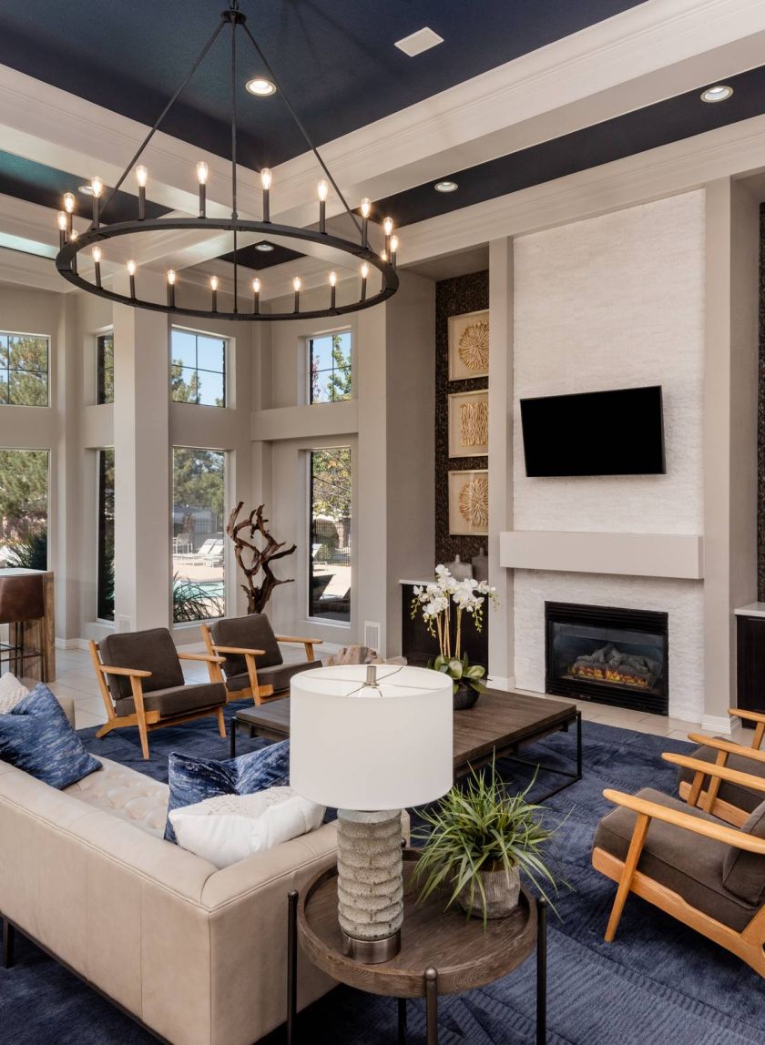 The Windsor modern common room with blue and beige decor, large windows, a fireplace, and stylish furniture including sofas and armchairs.