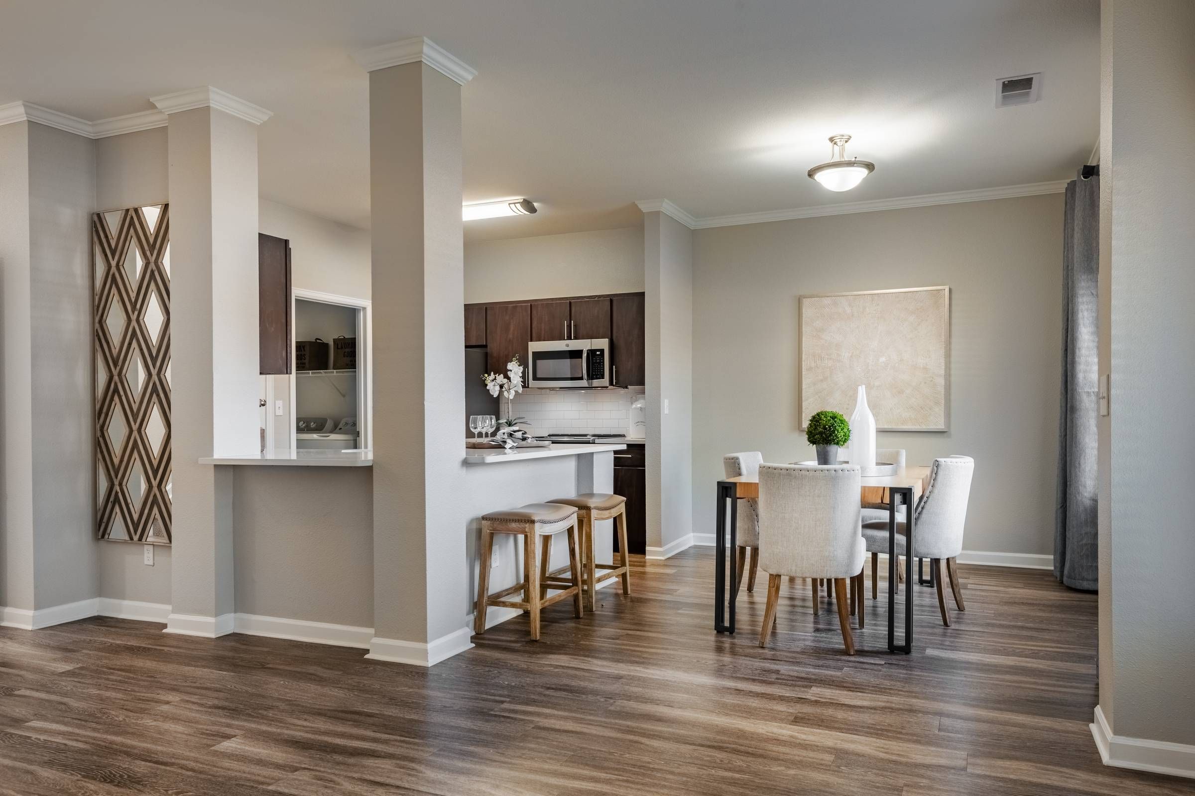 The Windsor modern dining and kitchen area with wood flooring, neutral walls, a dining table, and a kitchen with bar stools.