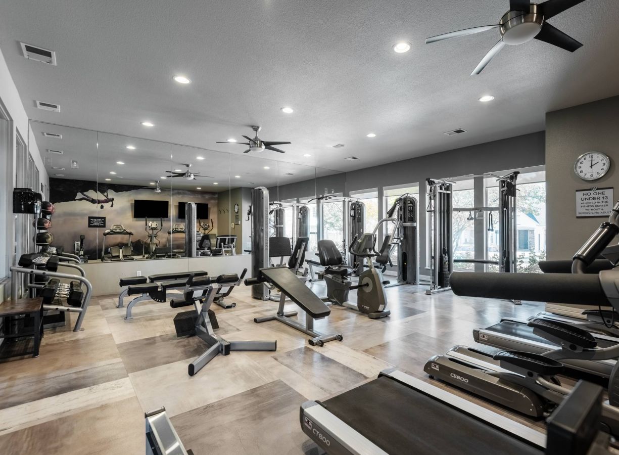 Brixton at Bear Creek modern gym with various cardio and strength equipment, mirrors, ceiling fans, and large windows allowing natural light in.