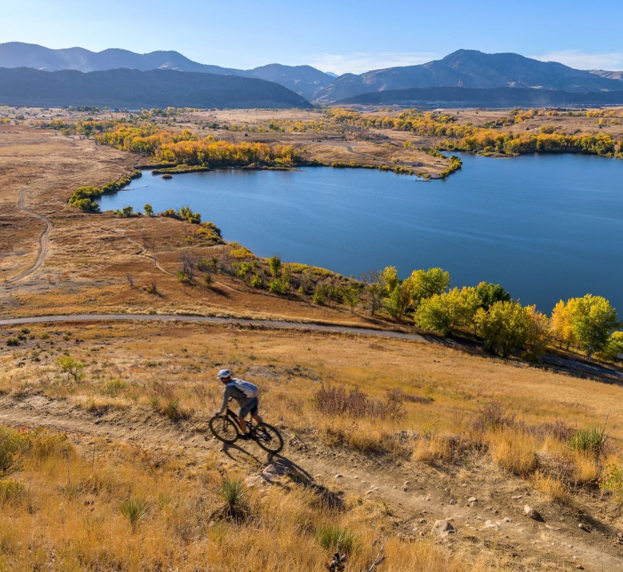 The Windsor resident cyclist riding on a trail overlooking a lake and mountains under a clear blue sky during fall.