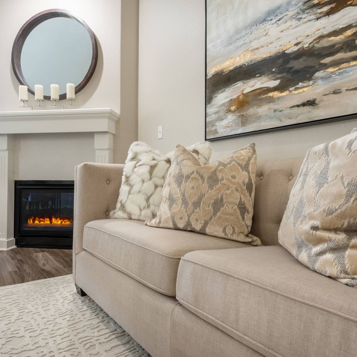 The Windsor cozy living room with a beige sofa adorned with pillows, a lit fireplace, and a large abstract painting on the wall.