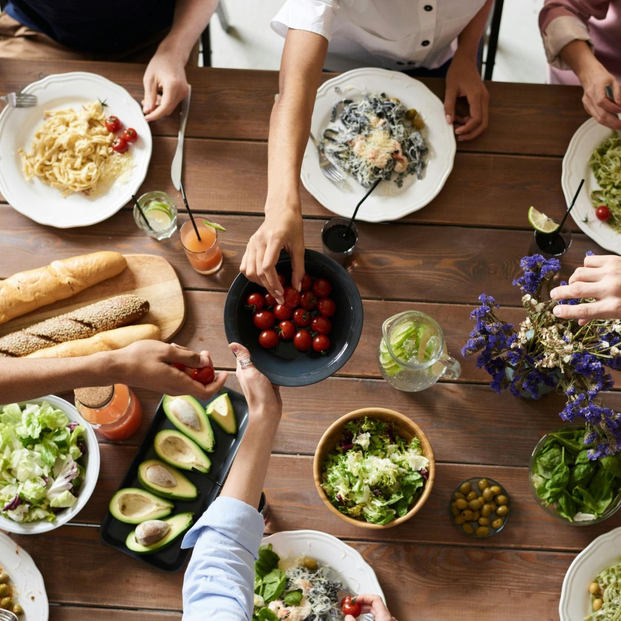 Group of people gathered around a wooden table, sharing a meal with various dishes, salads, and drinks.