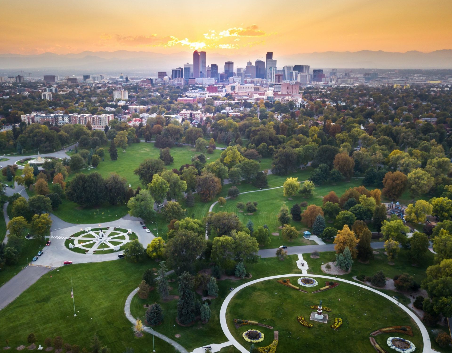 Aerial view of the Denver skyline at sunset with a large, green park in the foreground and mountains in the distance, near The Windsor luxury apartments.