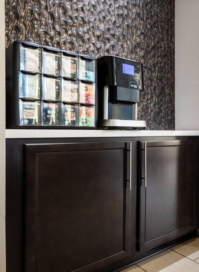 Brixton at Bear Creek office break room with a coffee machine and assorted coffee pods on a counter, adjacent to a spacious white-tiled lobby.