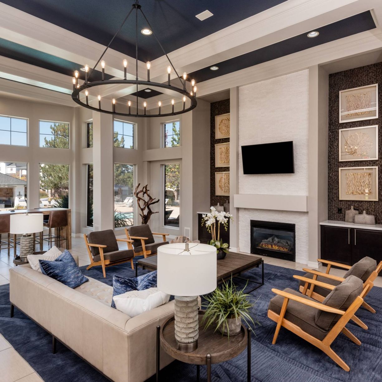 The Windsor modern common room with blue and beige decor, large windows, a fireplace, and stylish furniture including sofas and armchairs.